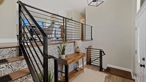 A staircase with black railings, a wooden console table, and patterned floor tiles. - Nestled in the beautiful desert of Tucson, this home will take your breath away. (Tucson)
