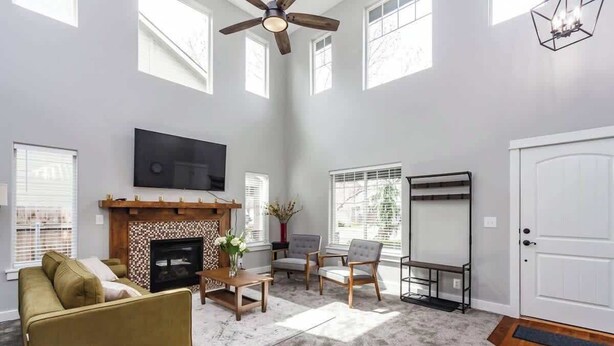 A spacious living room with a fireplace, a ceiling fan, and a large TV. - Upscale House for up to 20 with Fire Pit & Pool (Meridian)