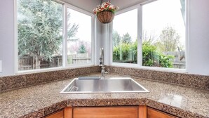 A kitchen with granite countertops, a stainless steel sink, wooden cabinets, and a hanging flower basket. - Upscale House for up to 20 with Fire Pit & Pool (Meridian)