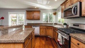 A modern kitchen with granite countertops, wooden cabinets, a stainless steel range, and a dishwasher. - Upscale House for up to 20 with Fire Pit & Pool (Meridian)