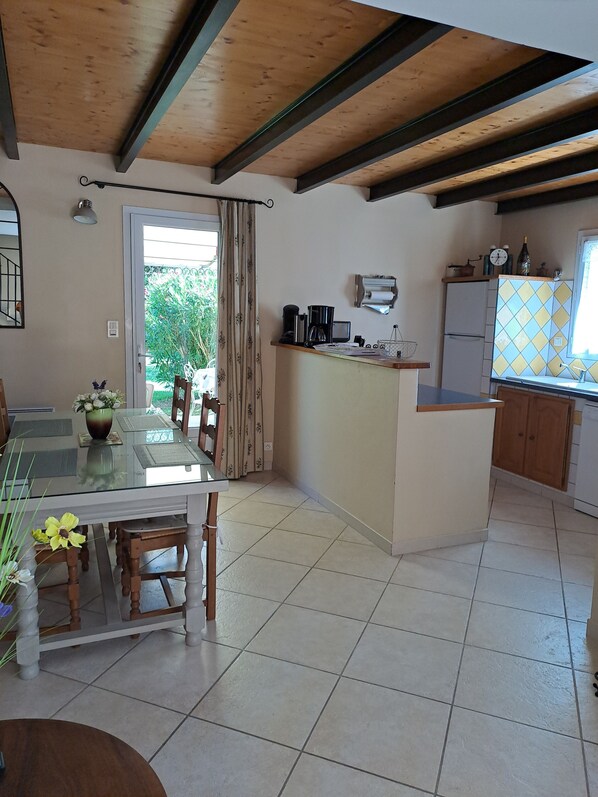 A kitchen with a dining area, wooden beams, tiled floor, and a window with curtains.