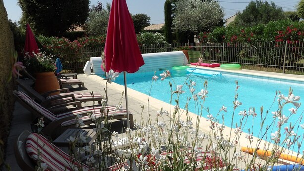 Une piscine entourée d’une clôture et agrémentée de divers végétaux, avec des chaises longues et des parasols.