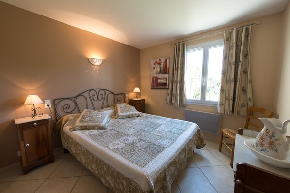 A bedroom with a bed, nightstands, a chair, and a window with curtains.