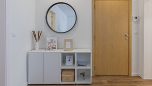 A hallway with a wooden door, a white console with shelves, a round mirror, and a wall-mounted thermostat. - An accomodation very close to Ponta Delgada! (Ponta Delgada)
