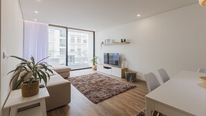 A modern living room with a sofa, a dining table, a TV, and a large window. - An accomodation very close to Ponta Delgada! (Ponta Delgada)