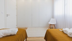 A hotel room with two beds, a white wardrobe, a white chair, and a window with sheer curtains. - An accomodation very close to Ponta Delgada! (Ponta Delgada)