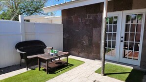 Une terrasse avec un barbecue, une table et une porte donnant sur un espace abrité.