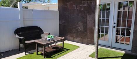 A patio with a grill, a table, and a door leading to a covered area.