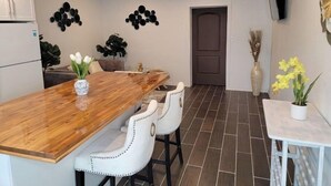 Une cuisine moderne avec une table à manger en bois, des chaises blanches, un réfrigérateur et des œuvres d’art décoratives au mur.