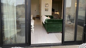 A room with a green sofa, a white chair, and a small table. There is a sliding glass door leading to an outdoor area. - Asylum 58 Condo @ Grand Traverse Commons (Traverse City)