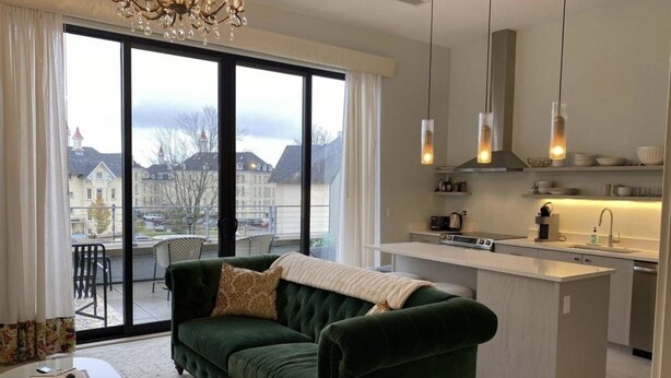 A modern living room with a green sofa, a small coffee table, and a view of a cityscape through large windows. - Asylum 58 Condo @ Grand Traverse Commons (Traverse City)