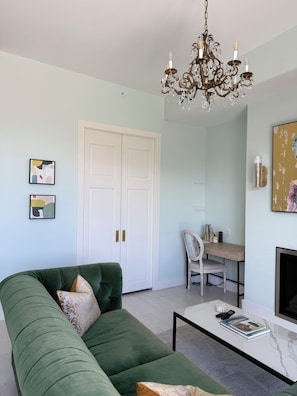 A living room with a green sofa, a white coffee table, a chandelier, and a fireplace. - Asylum 58 Condo @ Grand Traverse Commons (Traverse City)