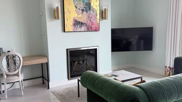 A living room with a green sofa, a fireplace, a flat-screen TV, and a chandelier.