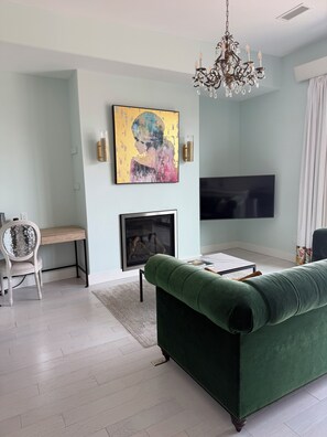 A living room with a green sofa, a fireplace, a flat-screen TV, and a chandelier.