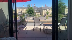 Een balkon met een rode parasol, metalen stoelen en een ronde tafel.