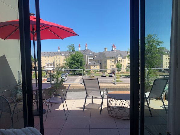 Un balcon avec un parasol rouge, des chaises en métal et une table ronde.
