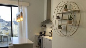 A modern kitchen with a central island, stainless steel appliances, and a built-in oven. There is a large window providing natural light and a view of the outside. - Asylum 58 Condo @ Grand Traverse Commons (Traverse City)