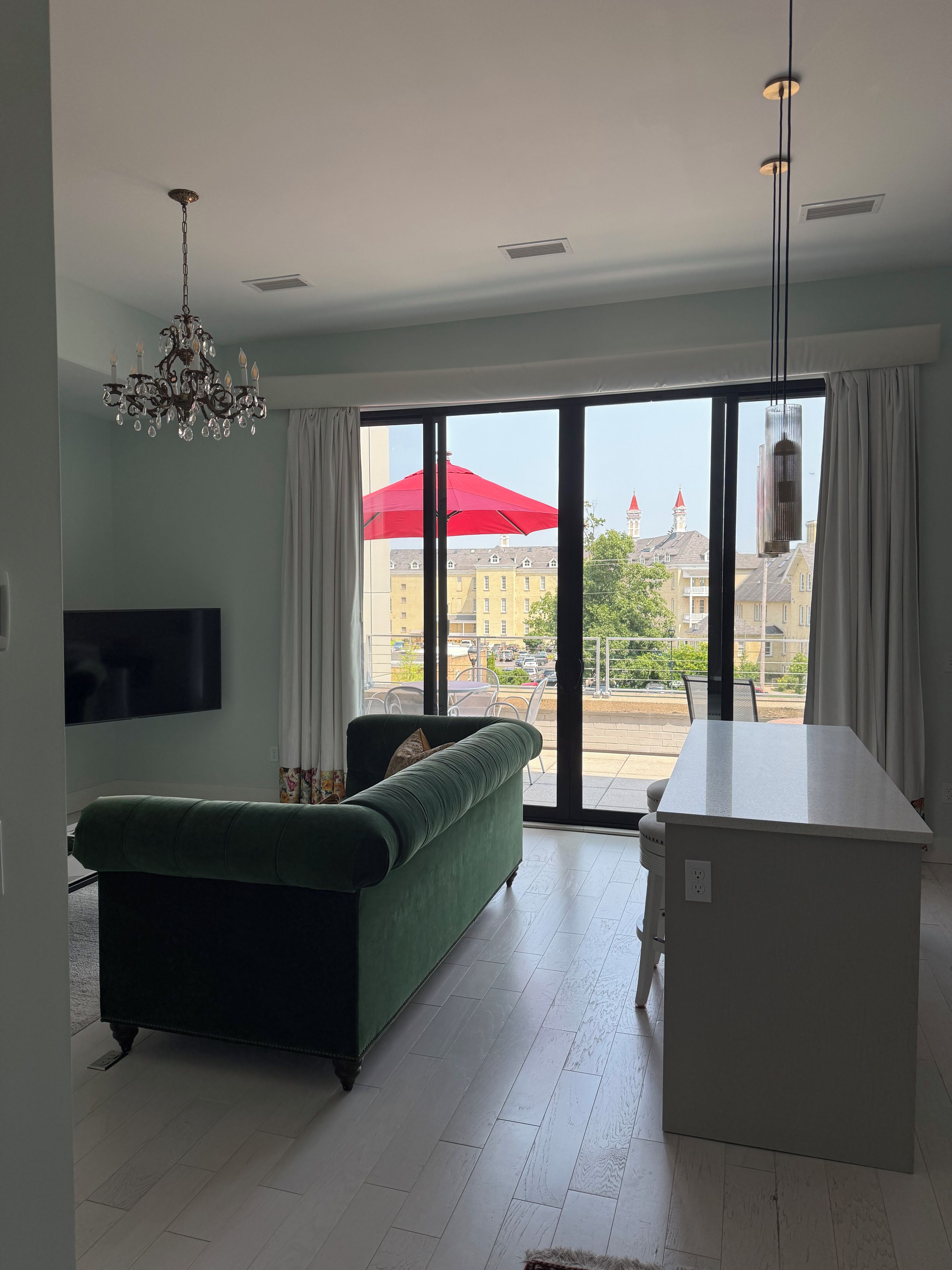 A modern living room with a green sofa, a flat-screen TV, and a large sliding glass door leading to an outdoor area.