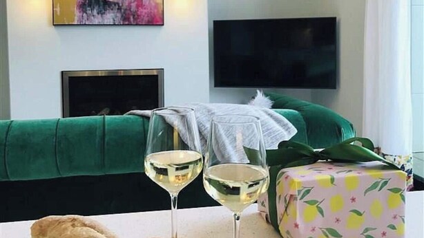 Een woonkamer met een groene bank, een flatscreen televisie aan de muur en twee wijnglazen op een tafel.