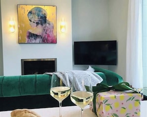 Un salon avec un canapé vert, un téléviseur à écran plat fixé au mur et deux verres à vin posés sur une table.