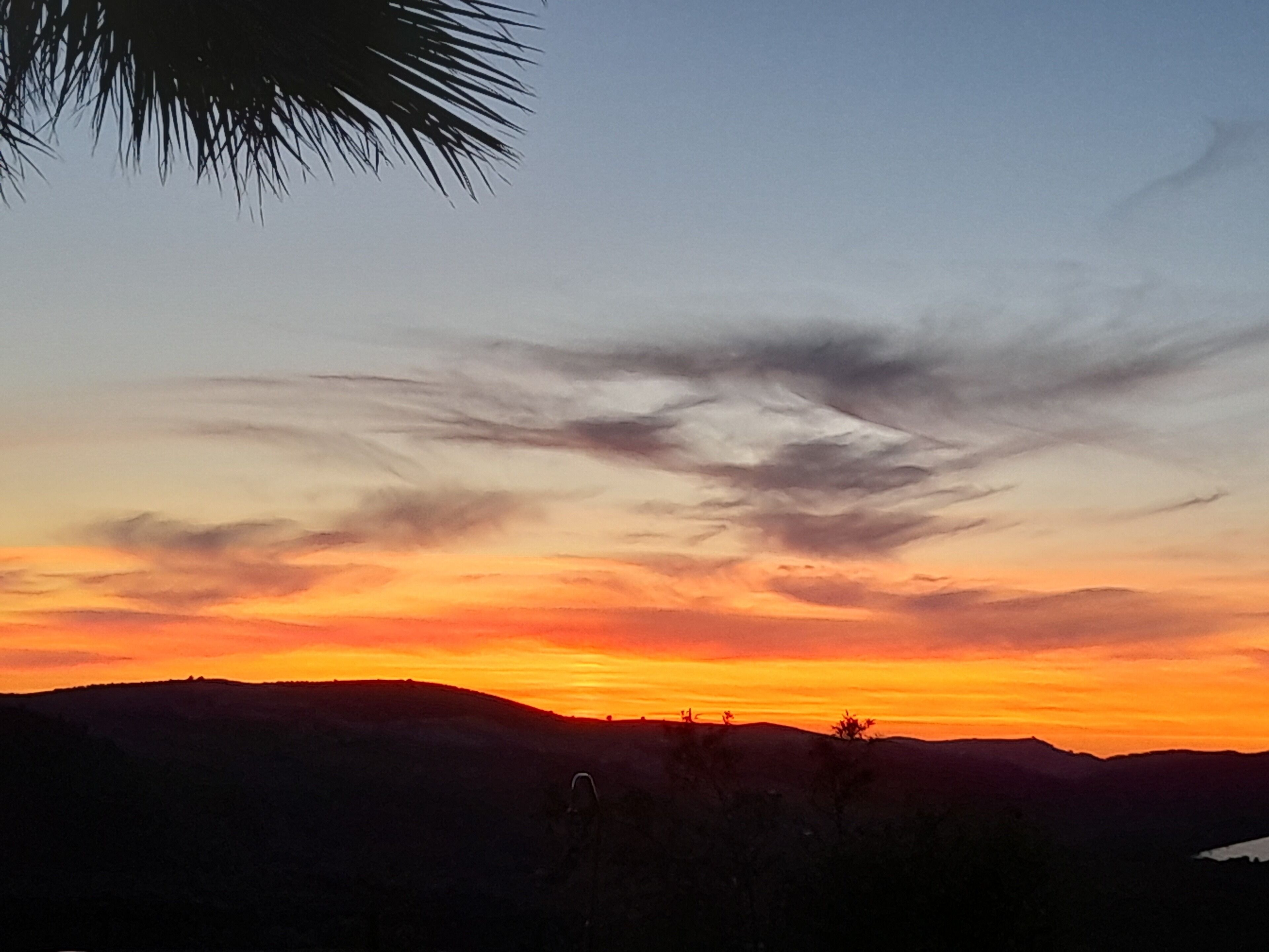 A sunset over a hilly landscape with silhouettes of trees and hills.