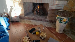A living room with a brick fireplace, a blue sofa, a coffee table with remote controls, a glass of orange juice, and a decorative vase.