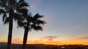 A pool area with a sunset view, palm trees, and distant mountains.
