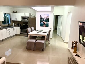 Una cocina moderna con armarios blancos, una mesa de comedor con sillas y un ventanal grande.