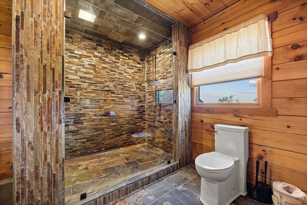 Un bagno con parete in pietra, cabina doccia in vetro e servizi igienici.