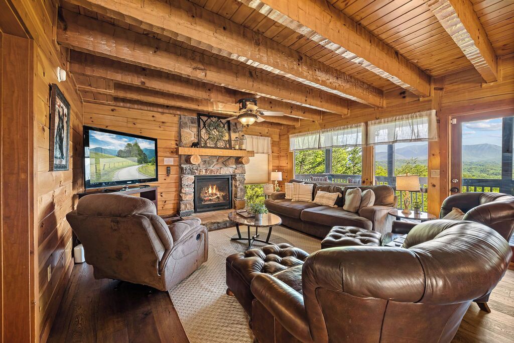 A cozy log cabin interior with a fireplace, leather furniture, and a television.
