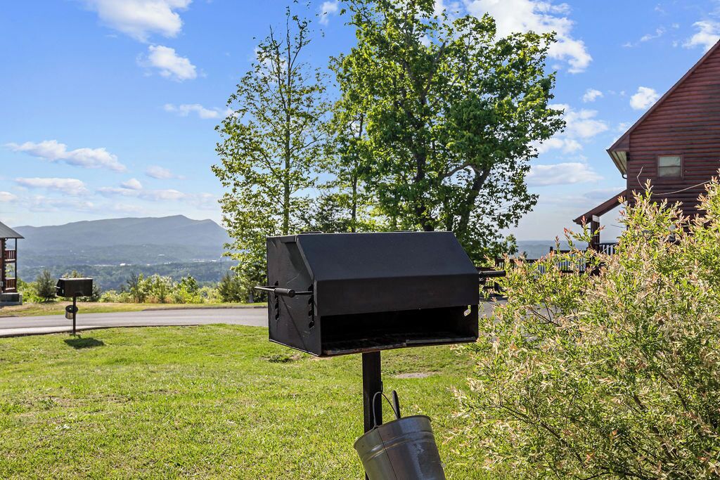 A barbecue grill in a grassy area with a house and mountains in the background.
