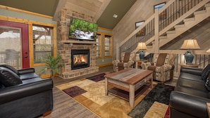 A spacious living room with a stone fireplace, leather sofas, a wooden coffee table, and a staircase with a railing. - Serenity Peak (Gatlinburg)