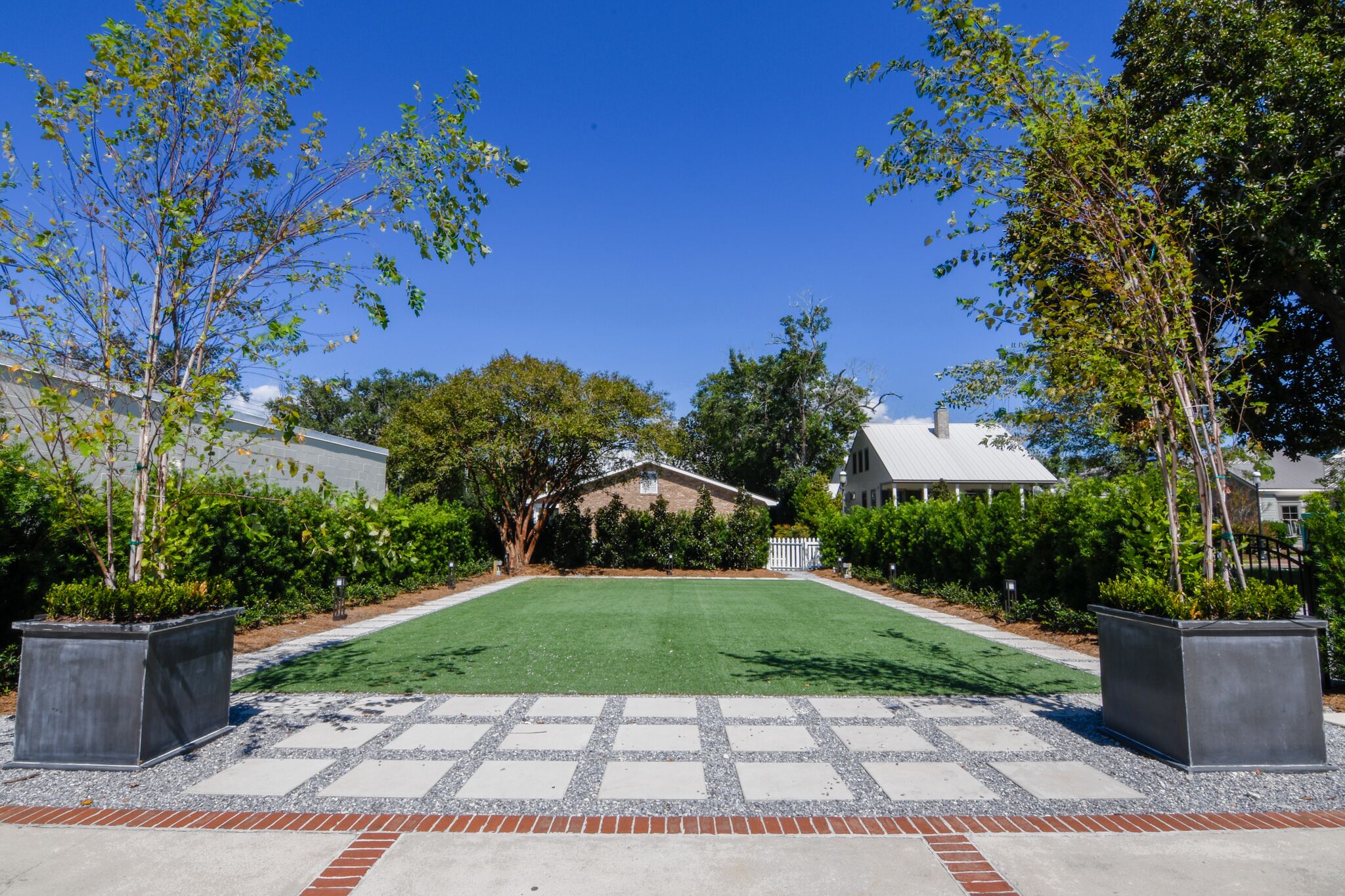 A well-maintained lawn with a paved walkway leading to a house with a white fence and a covered porch.