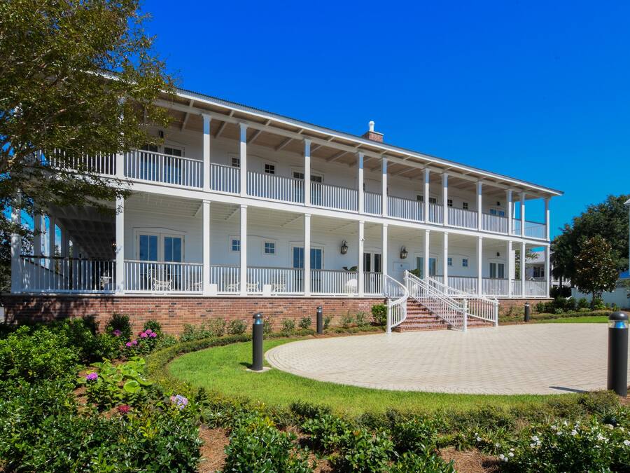 A two-story building with a covered balcony, brick foundation, and a landscaped garden with flowers.