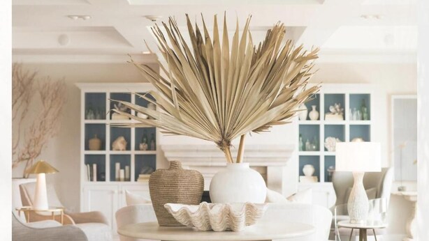 A well-lit room with a round table, a white vase with dried plants, and a decorative bowl.