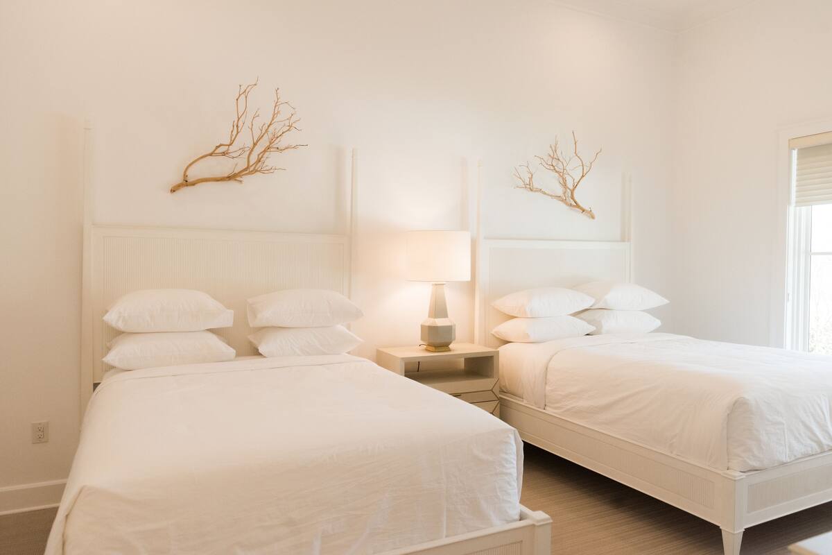 A hotel room with two single beds, a bedside table with a lamp, and wall-mounted branches.