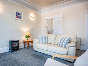 Una sala de estar con un sofá beige, una mesita con una lámpara, una chimenea y un espejo montado en la pared.