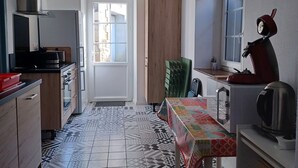 Kompakti keittiö, jossa on laattalattia, puinen kaappi, mikroaaltouuni, vedenkeitin ja pöytä, jonka päällä on värikäs pöytäliina.