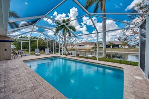 Relax by the pool surrounded by lush greenery and a serene body of water.