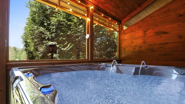 Un jacuzzi en una cabaña de madera con vistas a árboles a través de grandes ventanales.