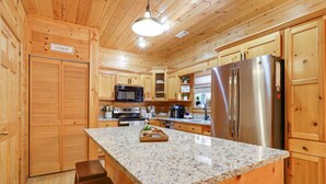 Una cocina con armarios de madera, encimera de granito, refrigerador de acero inoxidable y un microondas.