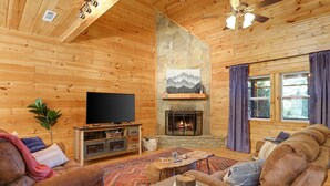 Un acogedor interior de cabaña de troncos con chimenea, paredes de madera, un televisor y asientos cómodos.