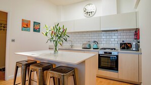 A modern kitchen with a central island, bar stools, a clock, and a toaster. - 2 bedroom accommodation in Newquay (Newquay)