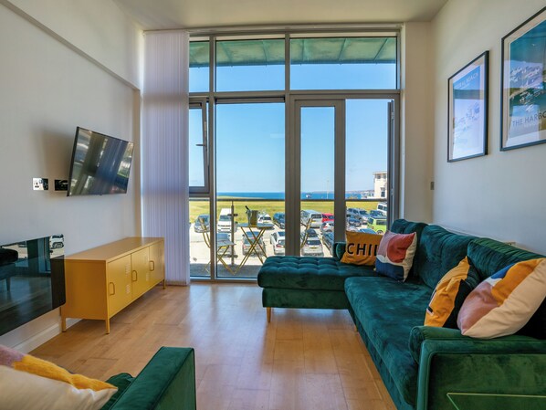 A modern living room with a green sofa, a yellow cabinet, and a TV on the wall.