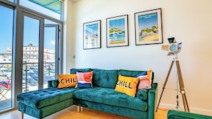 A modern living room with a green sectional sofa, two framed travel posters, and a vintage camera on a tripod. - 2 bedroom accommodation in Newquay (Newquay)