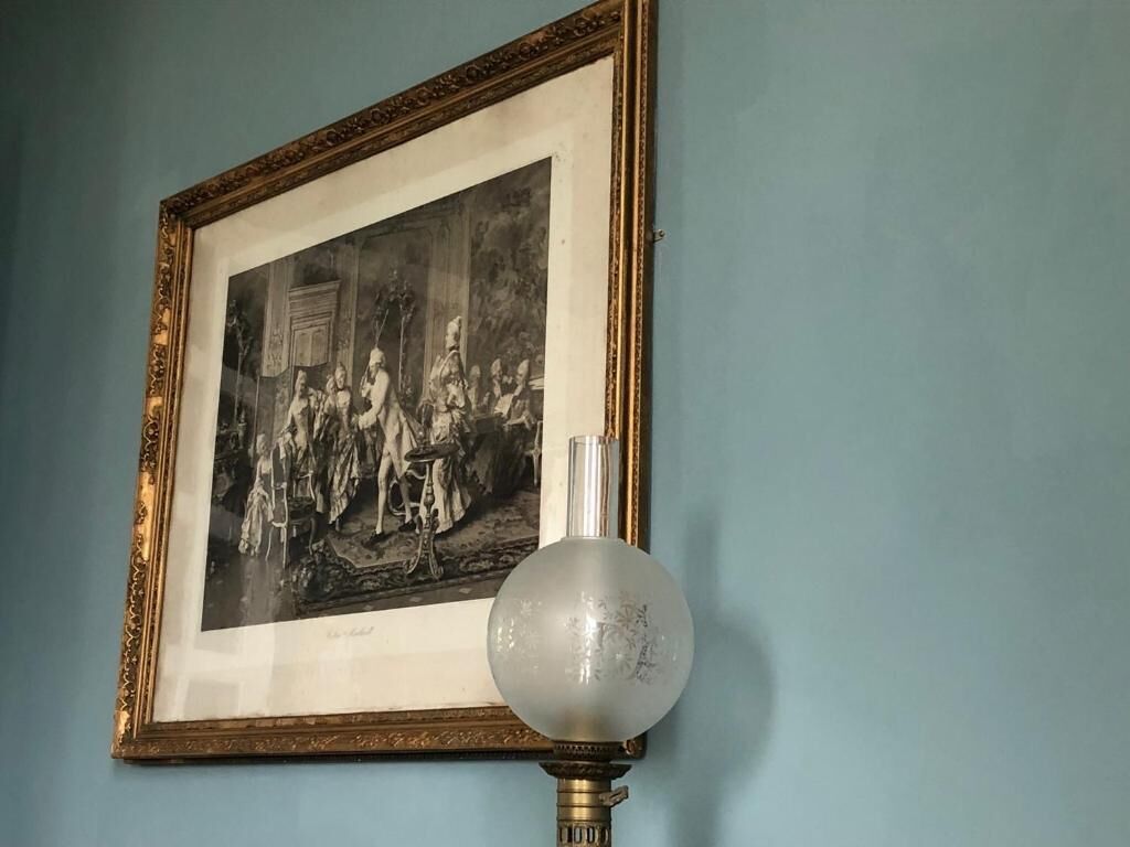 A framed black and white photograph on a wall, a vintage-style lamp with a clear glass shade, and a blue wall.