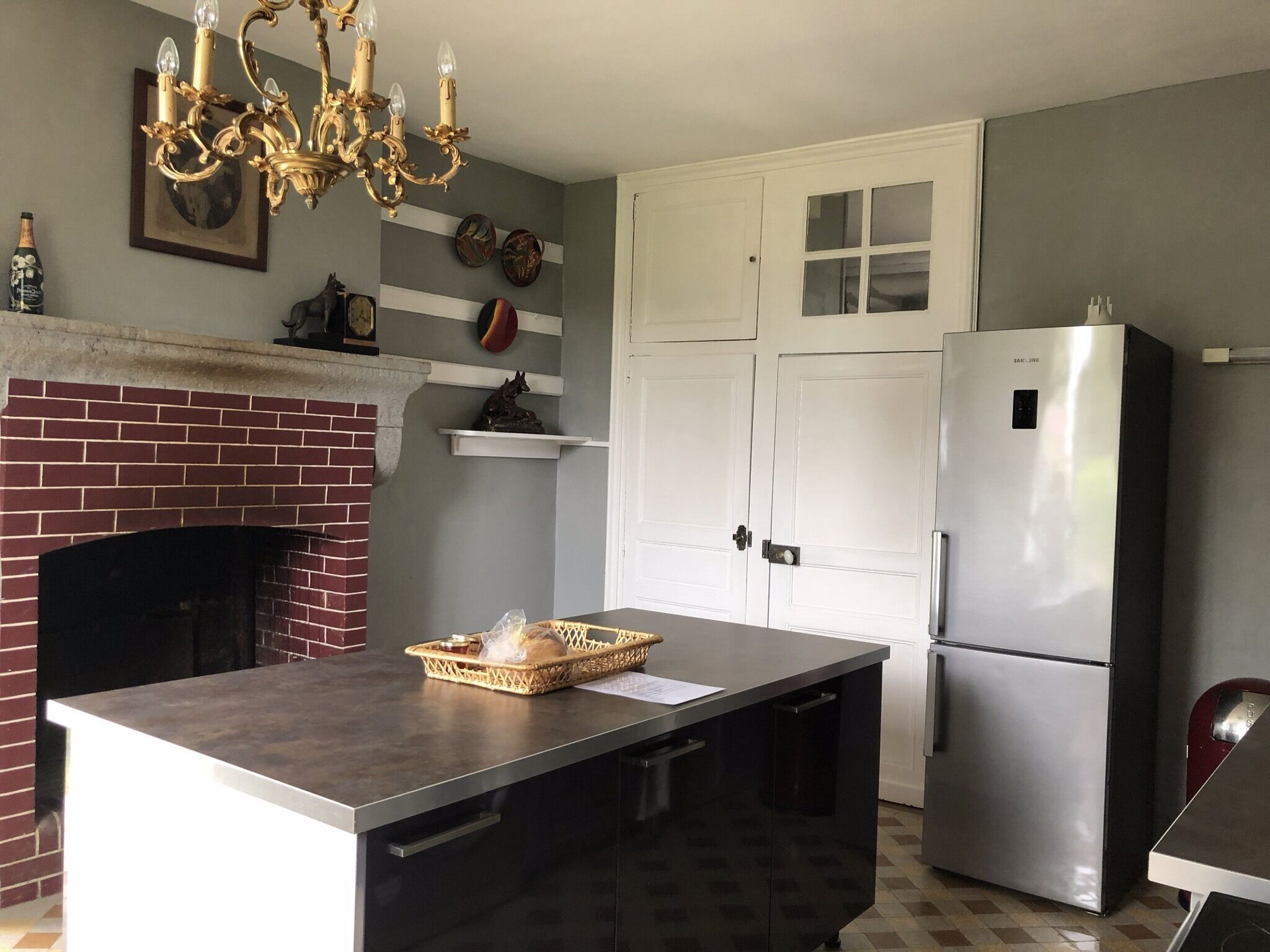 A kitchen with a brick fireplace, a stainless steel refrigerator, and a chandelier.