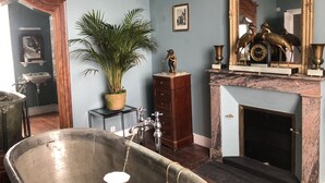 Ein Badezimmer im Vintage-Stil mit einer freistehenden Badewanne, einem Marmor-Kamin und einem großen Spiegel mit aufwendiger Goldfassung.