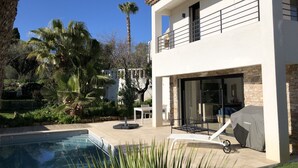 Ein modernes, zweistöckiges Haus mit Swimmingpool, Außenmöbeln und einer überdachten Terrasse.
