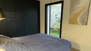 Ein Schlafzimmer mit einem Bett, einem dunklen Wandschrank, einem Fenster mit Blick auf Grünflächen und einem Bild an der Wand.